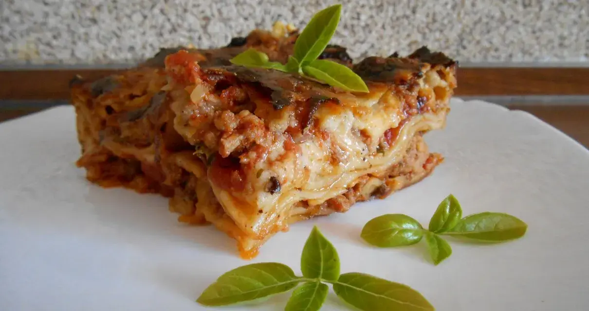 Kawałek pysznej lasagne z mięsem mielonym, udekorowany listkami bazylii. Prosty przepis na domową lasagne.