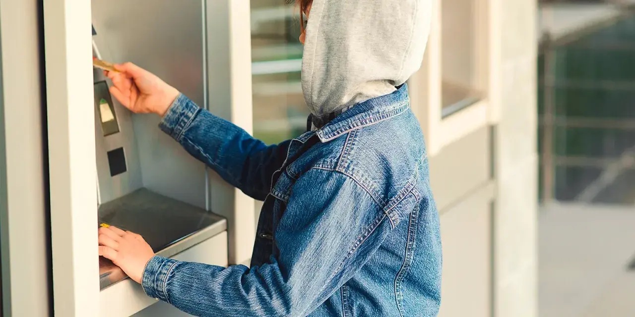 Jugendlicher mit Kapuze und Jeansjacke am Geldautomaten. Ein Beispiel für mögliche Verhaltensauffälligkeiten, die auf Kleptomanie bei Kindern hindeuten könnten.