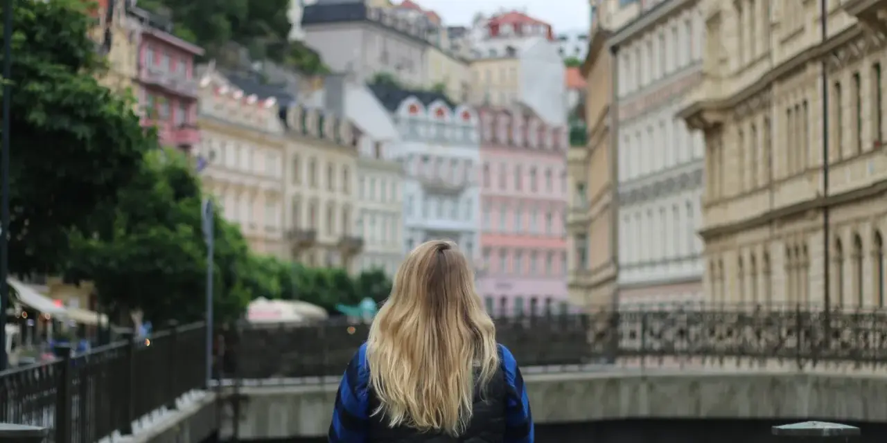 A woman with blonde hair gazes at colorful buildings, perhaps planning her day trips from Prague by train.