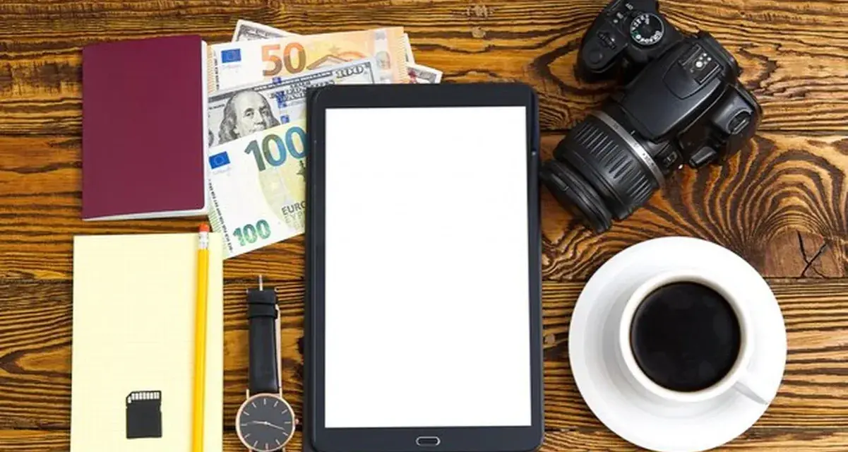 Planujesz podróż? Zastanawiasz się, ile kosztuje zdjęcie do dowodu u fotografa? Na zdjęciu paszport, pieniądze, aparat i tablet.
