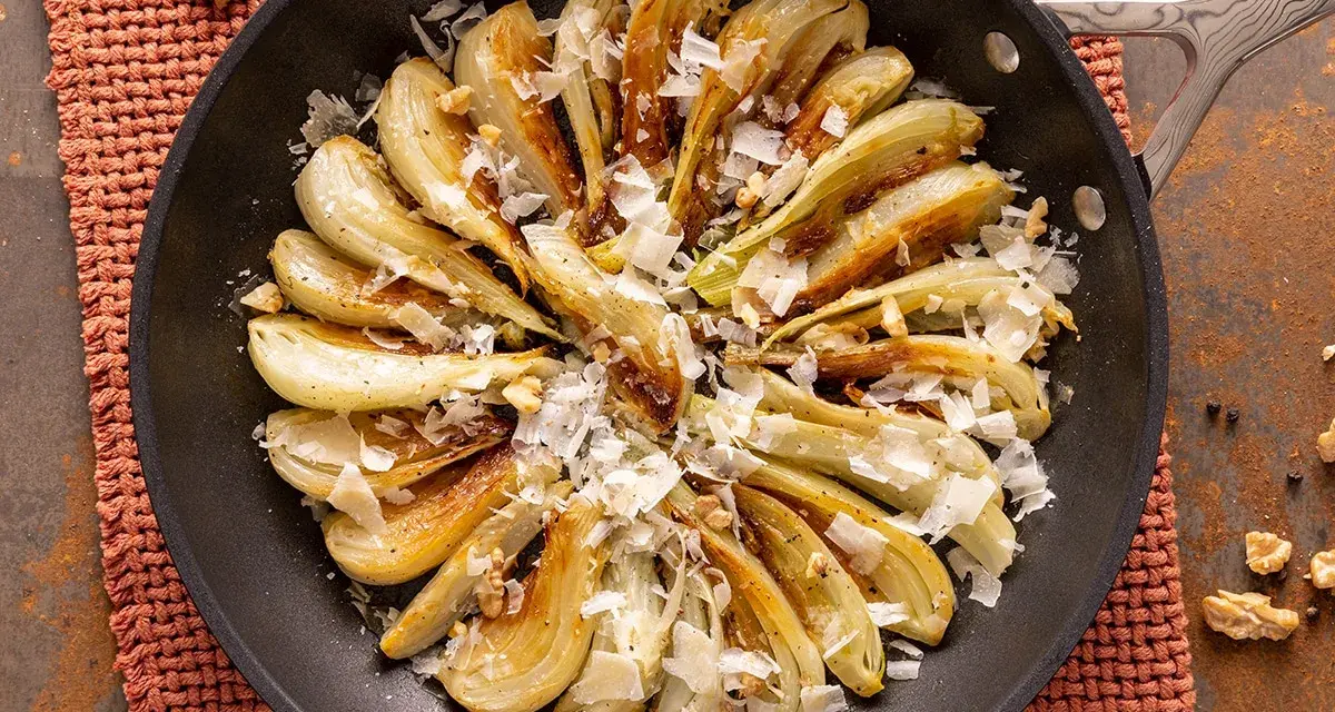Finocchi in padella dorati e saporiti, guarniti con scaglie di formaggio e noci croccanti.