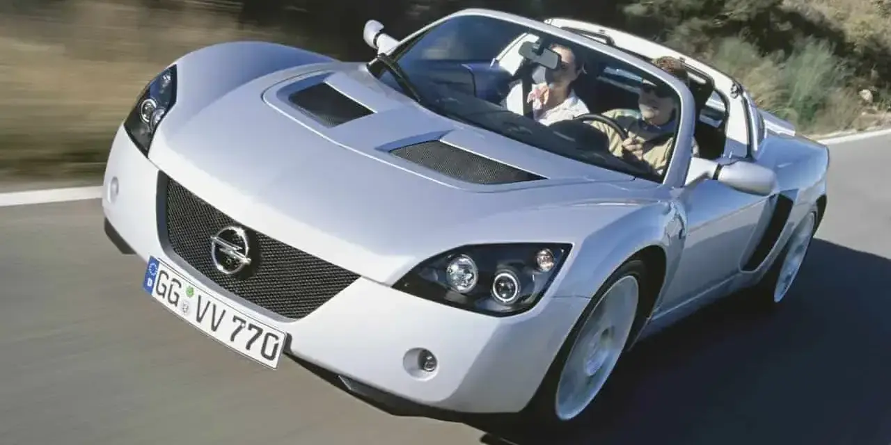 Srebrny Opel Speedster z dwoma pasażerami pędzi po krętej drodze.