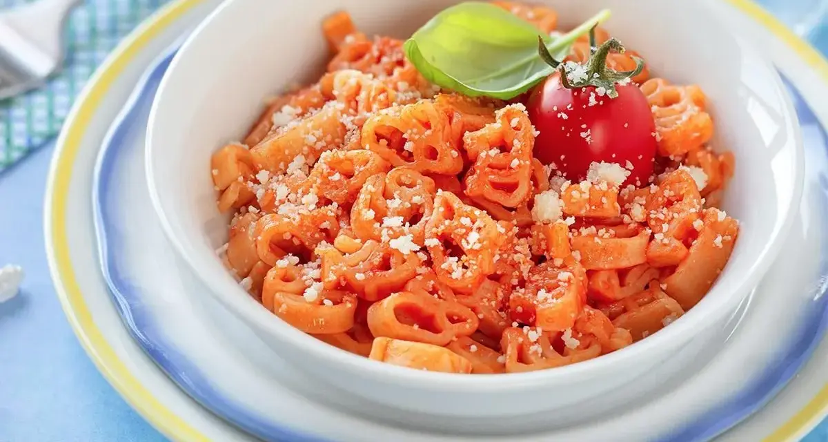Makaron w kształcie zwierzątek z sosem pomidorowym, posypany parmezanem, udekorowany pomidorkiem i bazylią.