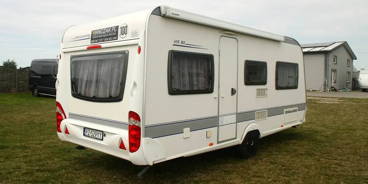 Biała przyczepa kempingowa Caravelair 495 RE na trawie, z widocznym logo MANCZAK.PL.