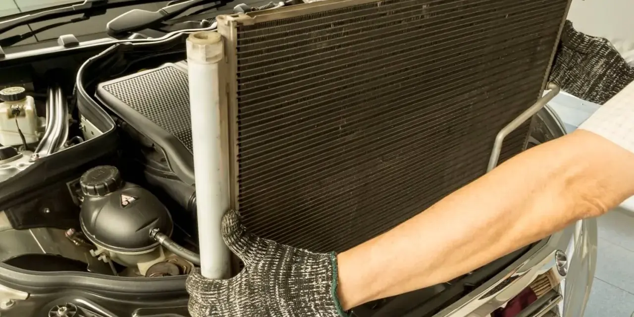 Mechanik w rękawicach wyjmuje chłodnicę klimatyzacji z silnika samochodu.