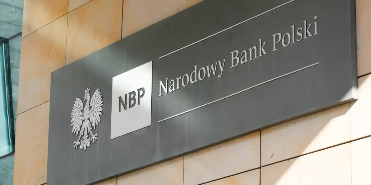 Tablica z godłem Polski i napisem "NBP Narodowy Bank Polski". Decyzje NBP wpływają na obniżkę stopy procentowej.