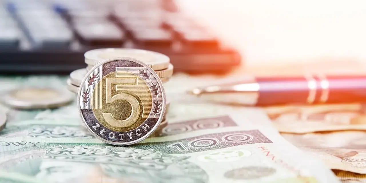 Złota moneta 5 złotych na stosie monet i banknotów. Obok długopis i kalkulator, sugerujące planowanie finansowe i możliwość recoverso rmc.