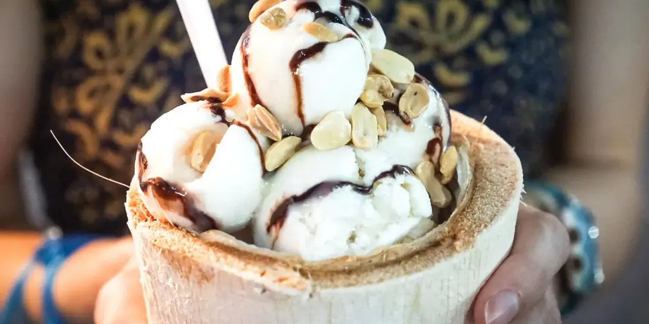 Cremiges Pina Colada Eis in einer Kokosnussschale, beträufelt mit Schokoladensauce und garniert mit Nüssen. Ein tropischer Genuss!
