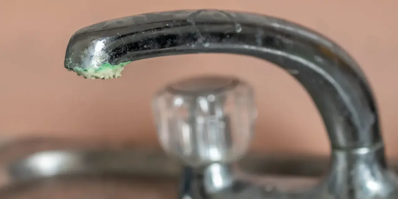 Robinet chromé avec un dépôt de calcaire vert de gris à son extrémité.