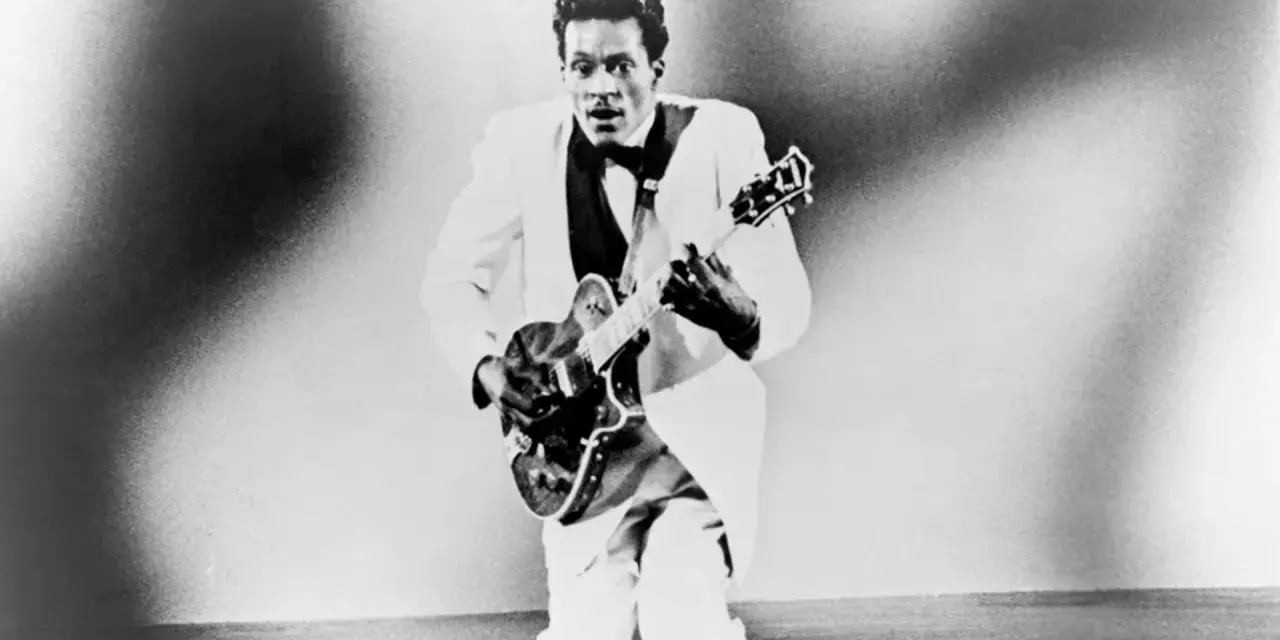 Chuck Berry in weißem Anzug spielt Gitarre, bereit für "Johnny B. Goode".