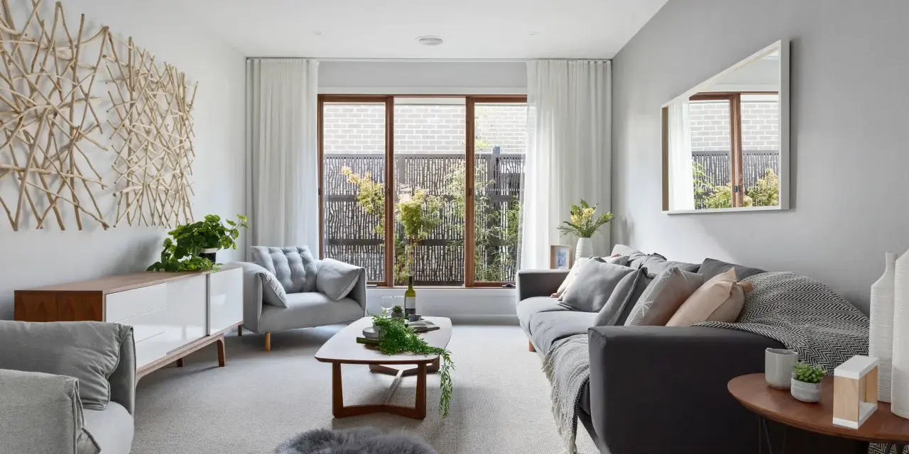 Sofá gris y sillón gris claro, con mesa de centro de madera. La decoración de ramas en la pared y la alfombra de piel gris crean un ambiente acogedor donde el beige y gris combinan a la perfección.