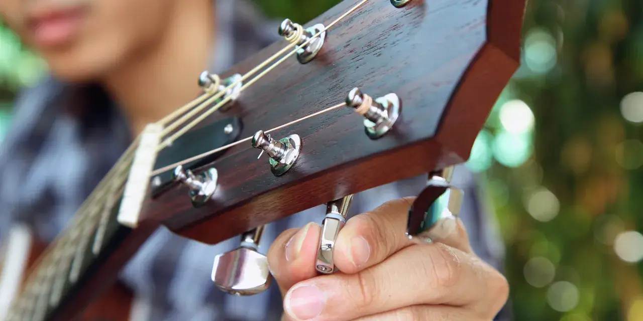 Nahaufnahme: Eine Hand stimmt eine 12-saitige Gitarre. Die Saiten sind gespannt, die Mechaniken glänzen.
