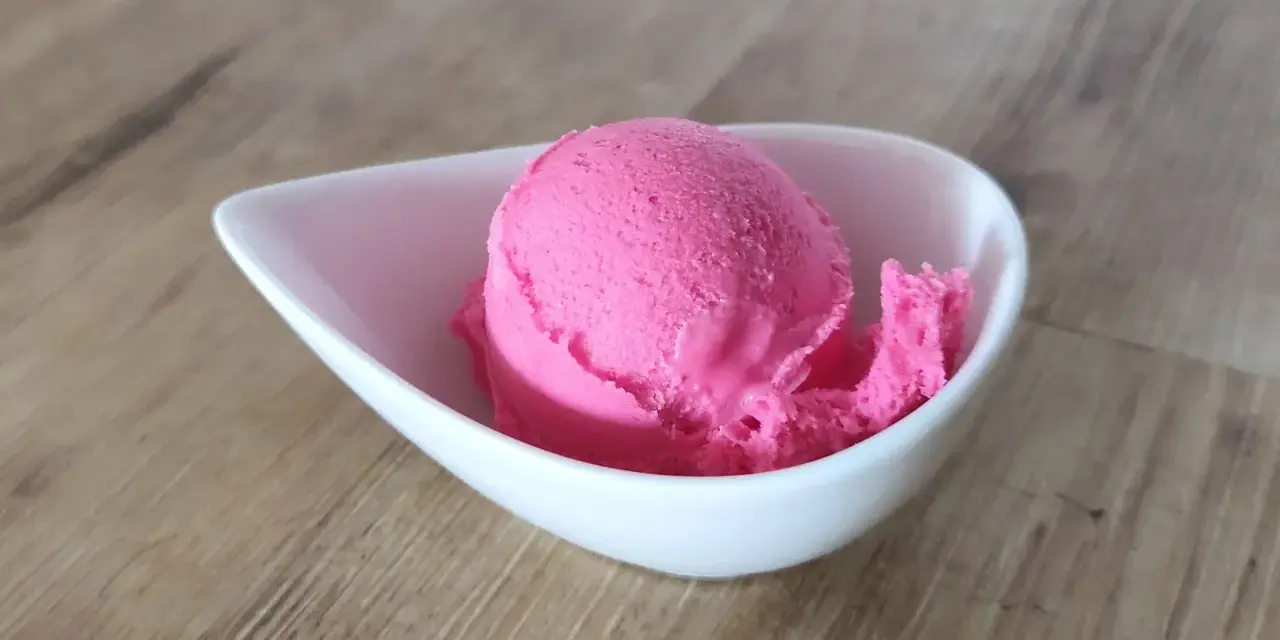 Ein Löffel leuchtend pinkes Eis in einer weißen Schale. Vielleicht ist das die Antwort auf die Frage, warum es kein Kirscheis gibt – weil dieses hier so gut ist!