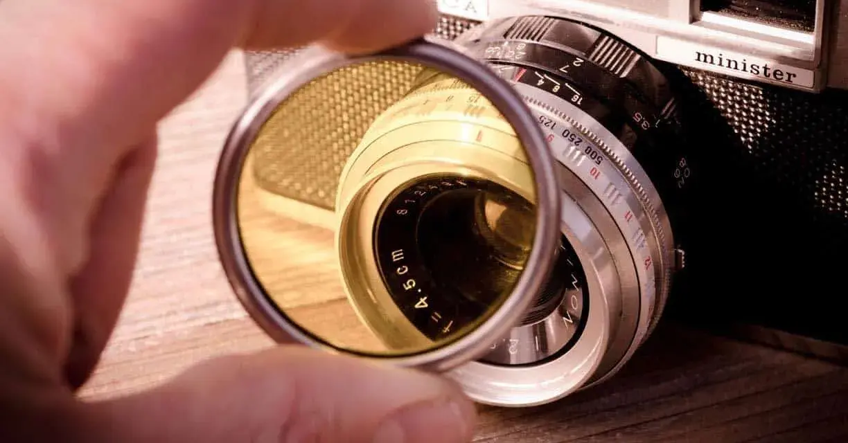 Une main tient un filtre protection objectif devant un vieil appareil photo argentique.