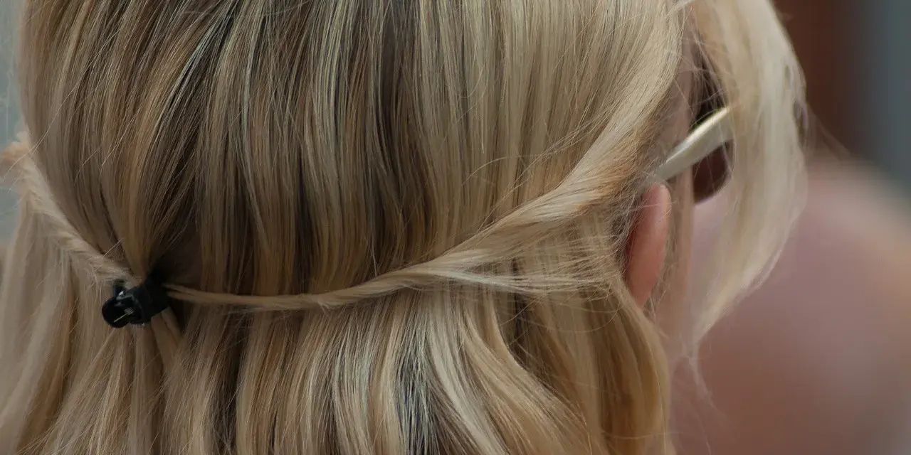 Piaskowy blond włosów spięty warkoczem z tyłu głowy. Delikatne pasma opadają na ramiona.