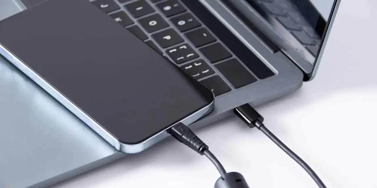 Ein iPhone wird über ein USB-C-Kabel mit einem Laptop verbunden, um Fotos zu übertragen.