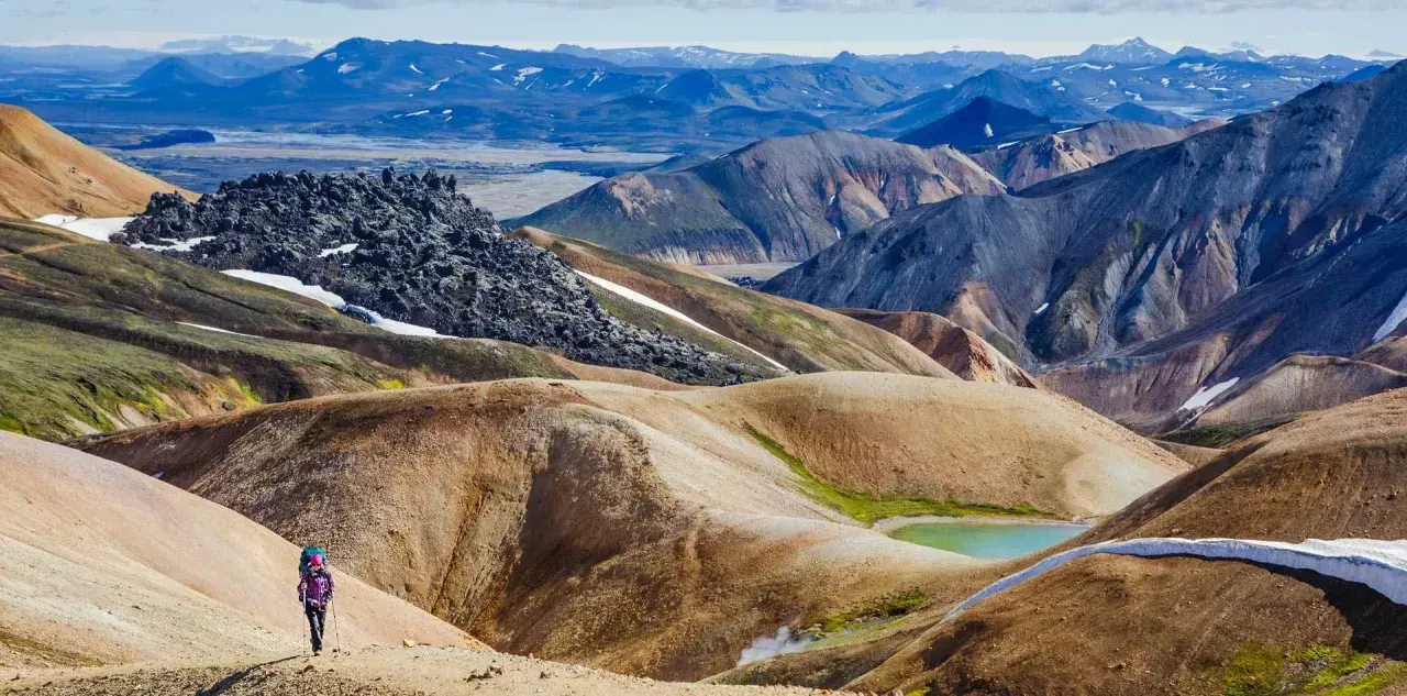 Un randonneur solitaire explore les paysages colorés et volcaniques de Landmannalaugar, un trek inoubliable en Islande.