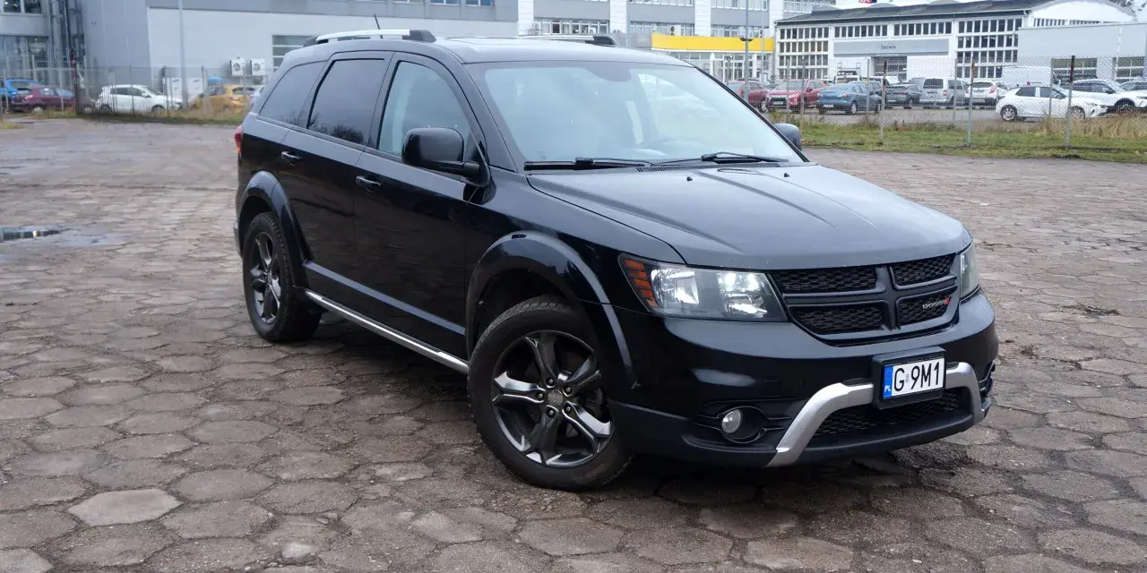 Czarny Dodge Journey 3.6 zaparkowany na placu z kostki brukowej. W tle budynki i inne samochody.