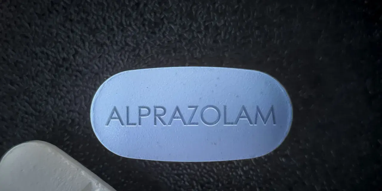 Niebieska tabletka z napisem "ALPRAZOLAM" leży obok białej. Uważaj na niebezpieczne skutki połączenia xanax i alkohol.
