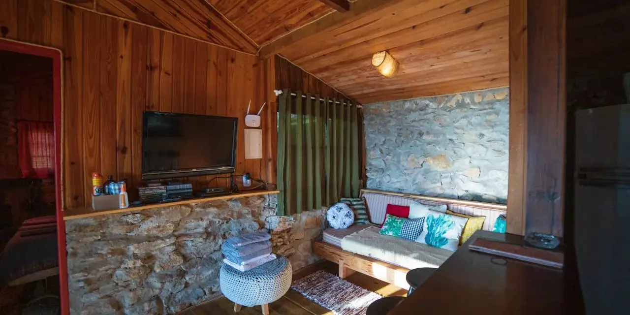 Un salon cosy en bois et pierre, avec canapé, TV et table. Idéal pour savoir comment agrandir une pièce avec style.