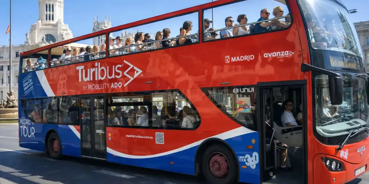 Tourists enjoy a hop on hop off bus tour of Madrid, Spain, with the iconic Turibus double-decker bus.