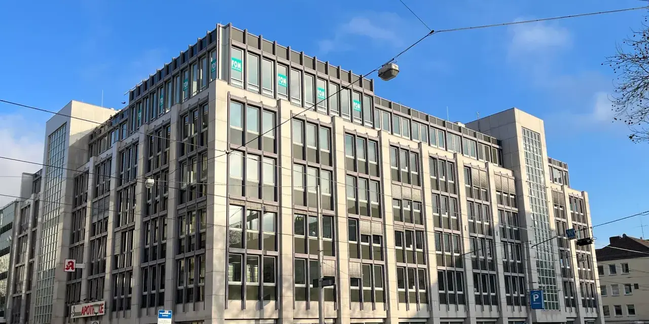 Modernes Bürogebäude in Kassel mit vielen Fenstern und "FOM"-Logos. Eine Apotheke ist im Erdgeschoss sichtbar.