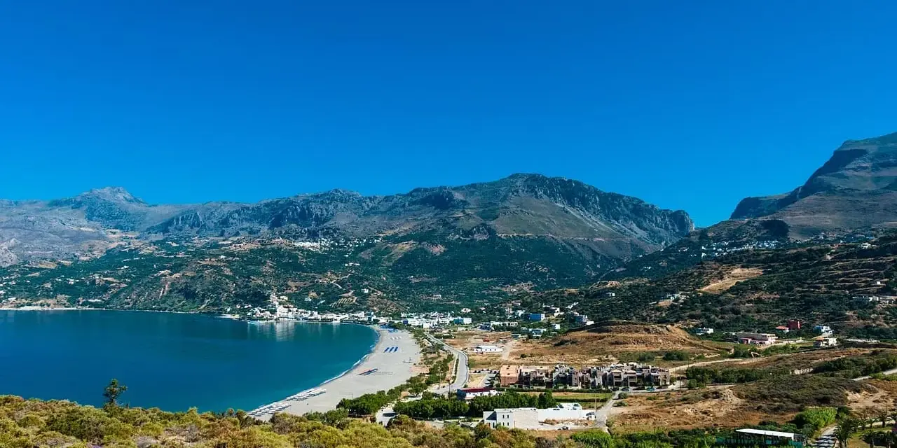 Malownicza zatoka z piaszczystą plażą i górami w tle. Urokliwe plaze Kreta zapraszają do odpoczynku.