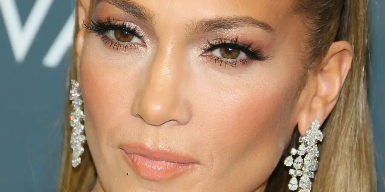 Nahaufnahme einer Frau mit auffälligem Make-up, braunen Augen, vollen Lippen und funkelnden Ohrringen.