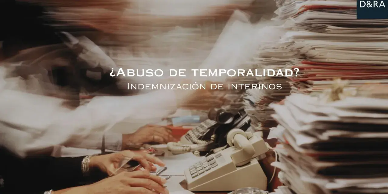 ¿Abuso de temporalidad? Indemnización de interinos tras 3 años. Escritorio caótico con papeles y teléfonos.
