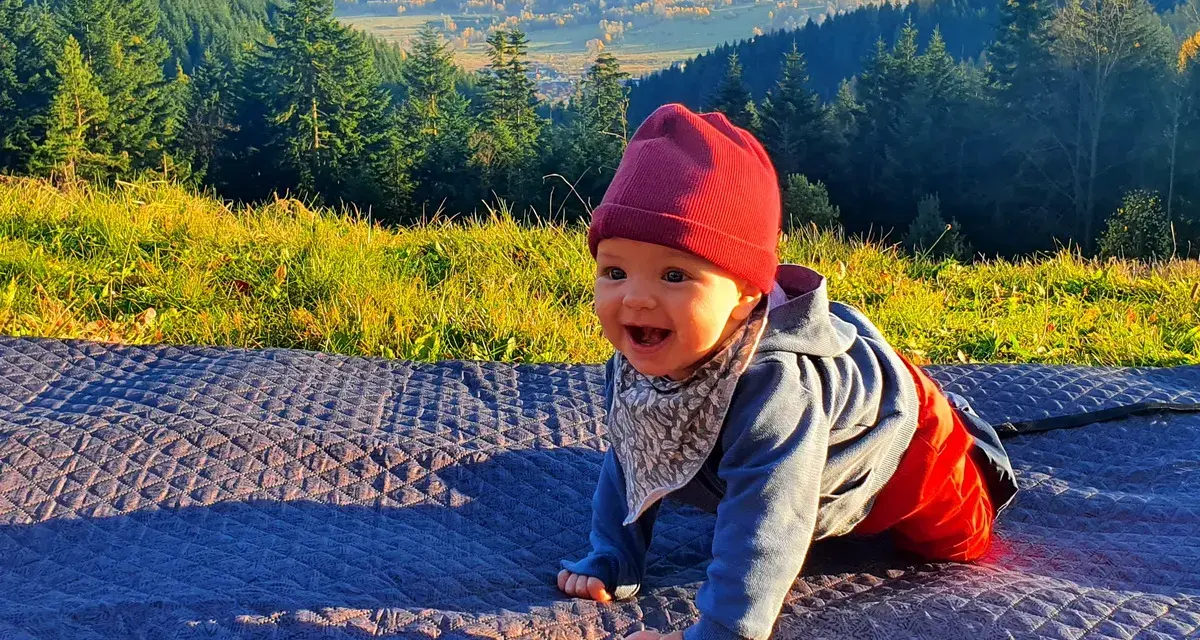 Uśmiechnięte dziecko na kocyku, w tle góry i las. Jakby czytało psalm 131 tekst o spokoju.