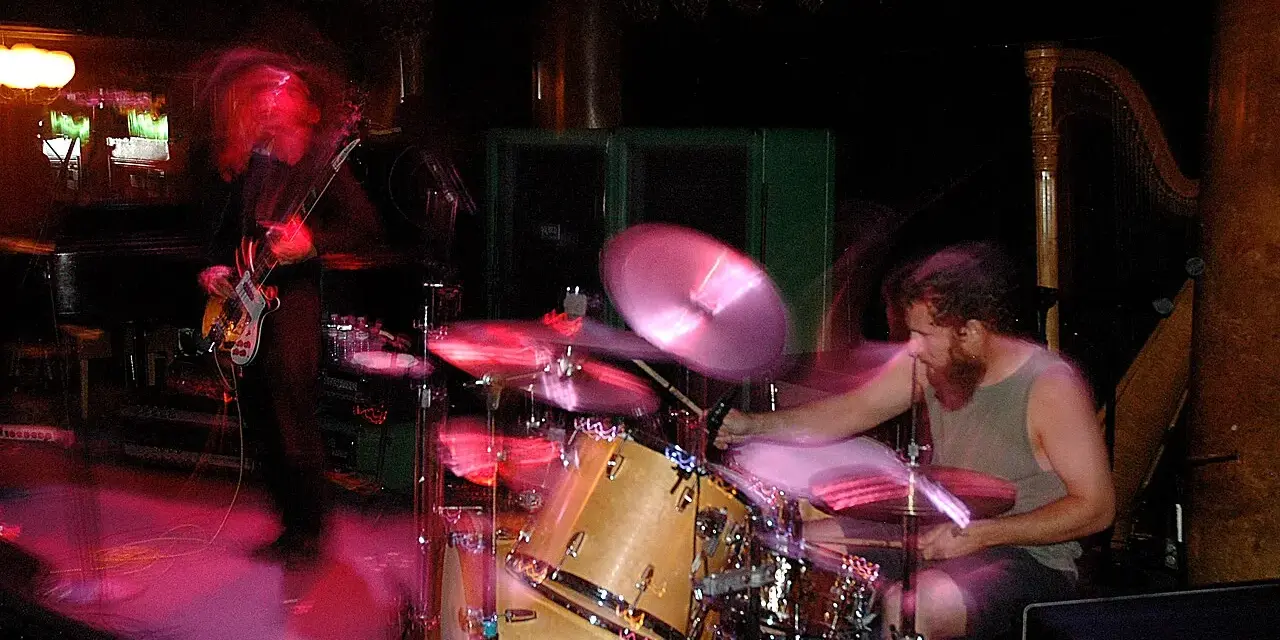 Ein Bassist und ein Schlagzeuger einer Stoner Rock Band in Aktion. Die Lichter und Bewegungen erzeugen eine dynamische Atmosphäre.