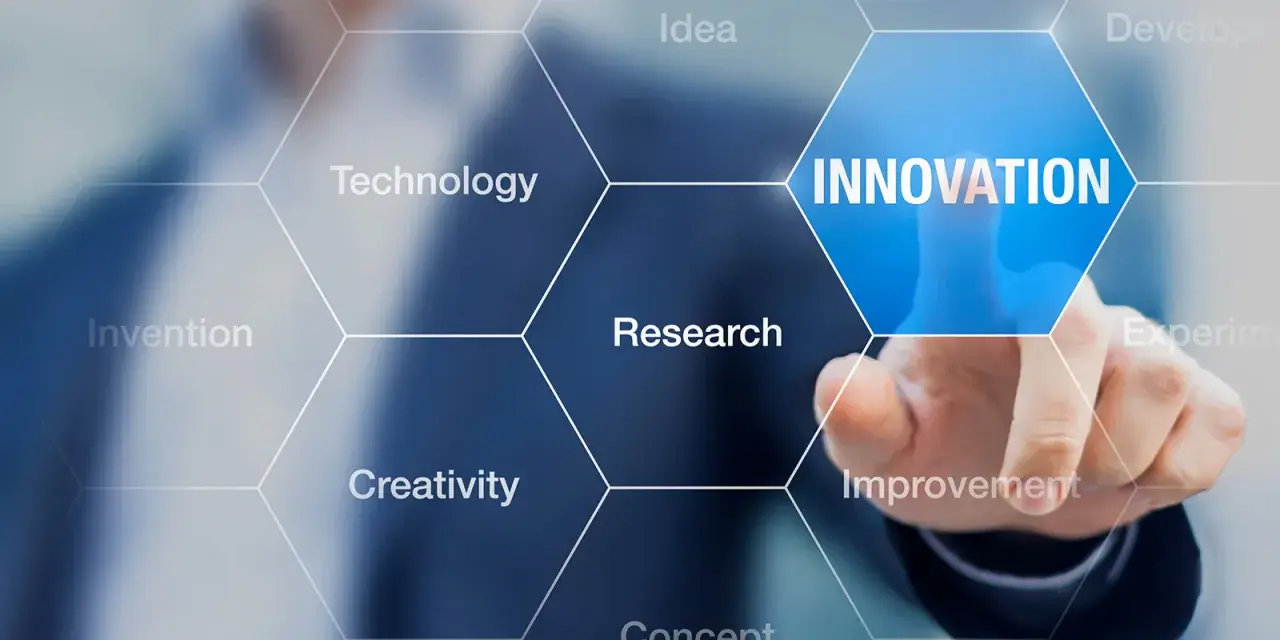 Dłoń dotyka ekranu z napisem "INNOVATION", otoczonego przez sześciokąty z hasłami: Idea, Technology, Research, Creativity, Invention, Improvement. To wizualizacja procesu, który może być częścią wzornictwo przemysłowe studia.