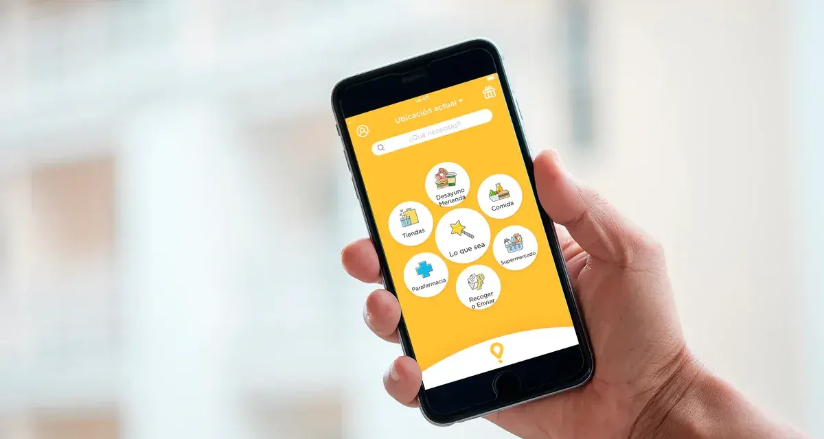 Mano sujetando un smartphone con una app de entregas. Muestra opciones como "Comida", "Supermercado" y "Parafarmacia". Así funciona "just eat".