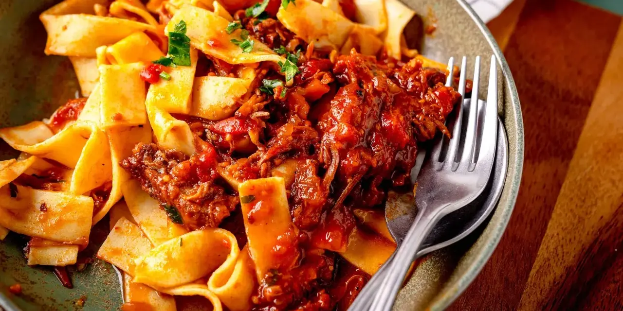 Breite Bandnudeln mit herzhaftem Ragu-Sauce, garniert mit frischer Petersilie. Ein Gabel liegt bereit.