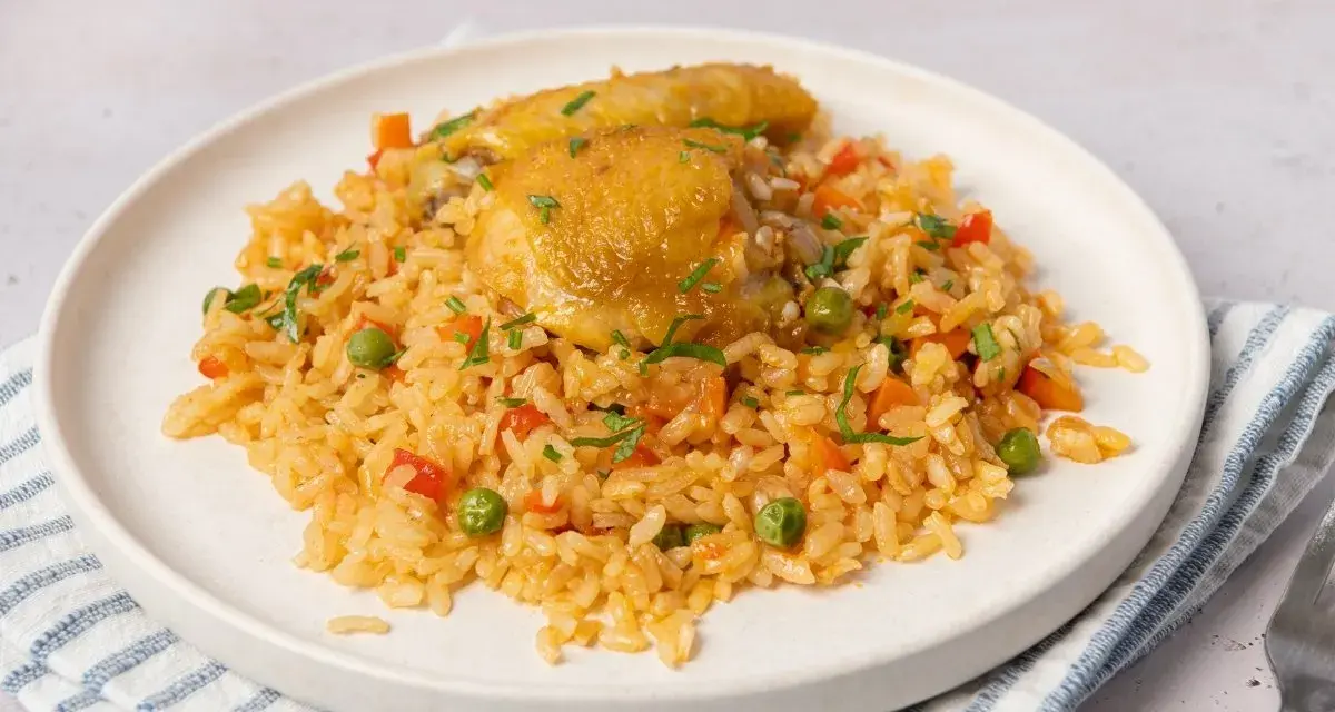 Arroz con pollo jugoso con verduras y perejil picado en un plato blanco.