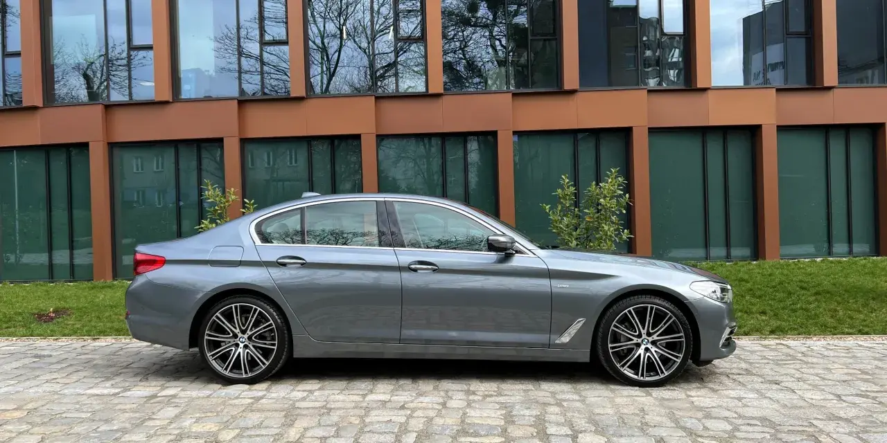 Szary sedan BMW G30 na tle nowoczesnego budynku.