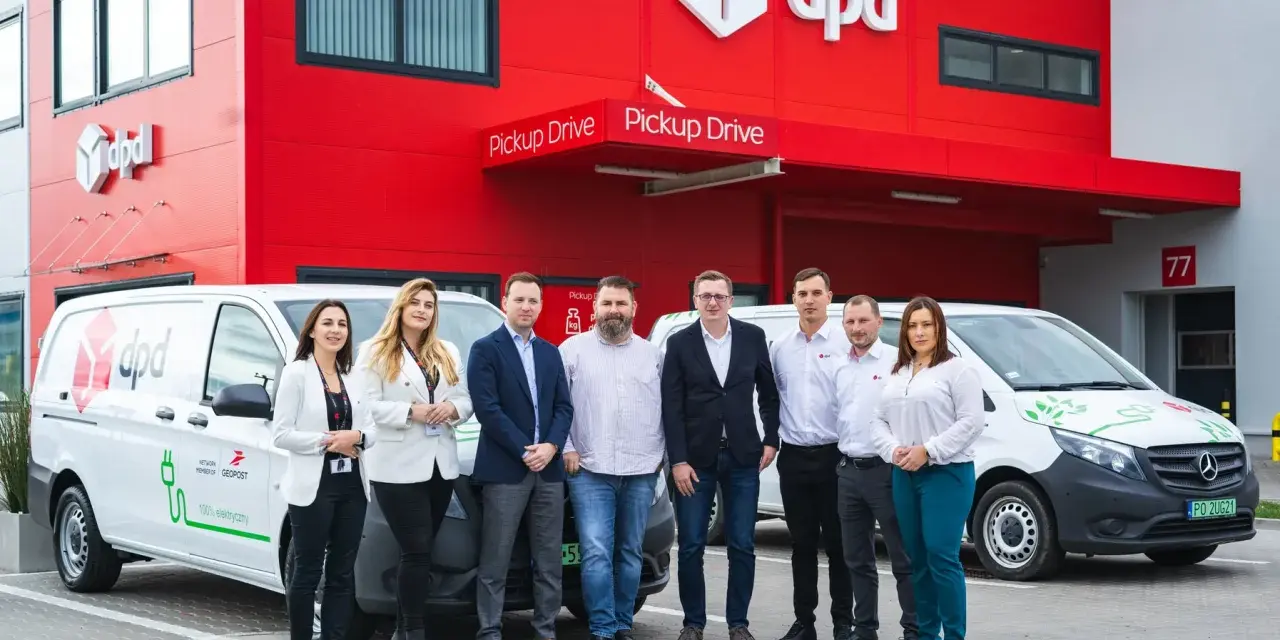 Zespół DPD pozuje przed budynkiem z logo firmy i elektrycznym dpd bus.