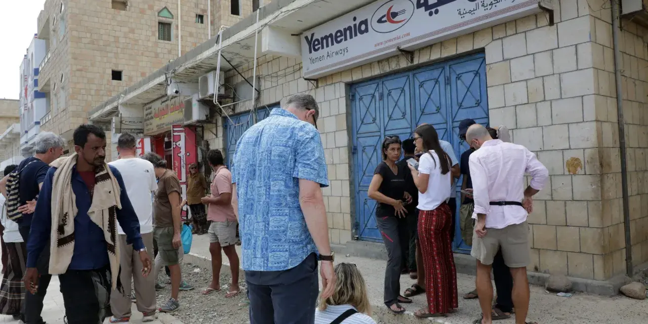Ludzie stoją przed biurem Yemenia Airways. Czy Jemen jest bezpieczny? To pytanie zadają sobie podróżni, obserwując codzienne życie w tym kraju.