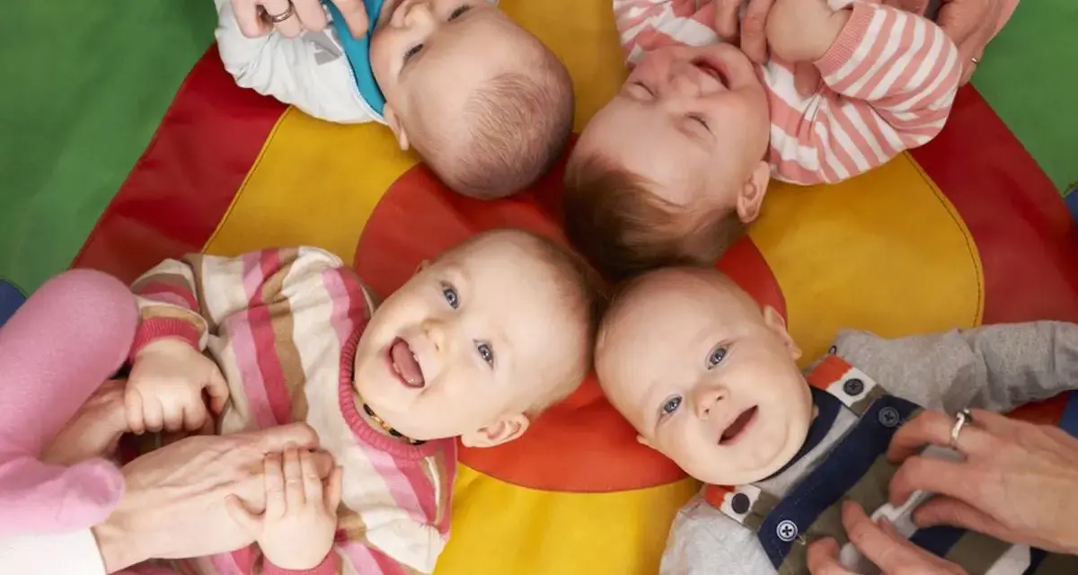 Uśmiechnięte dzieci na kolorowej macie. Czy żłobek jest dobry dla dziecka? Wiele maluchów wesoło bawi się z opiekunami.