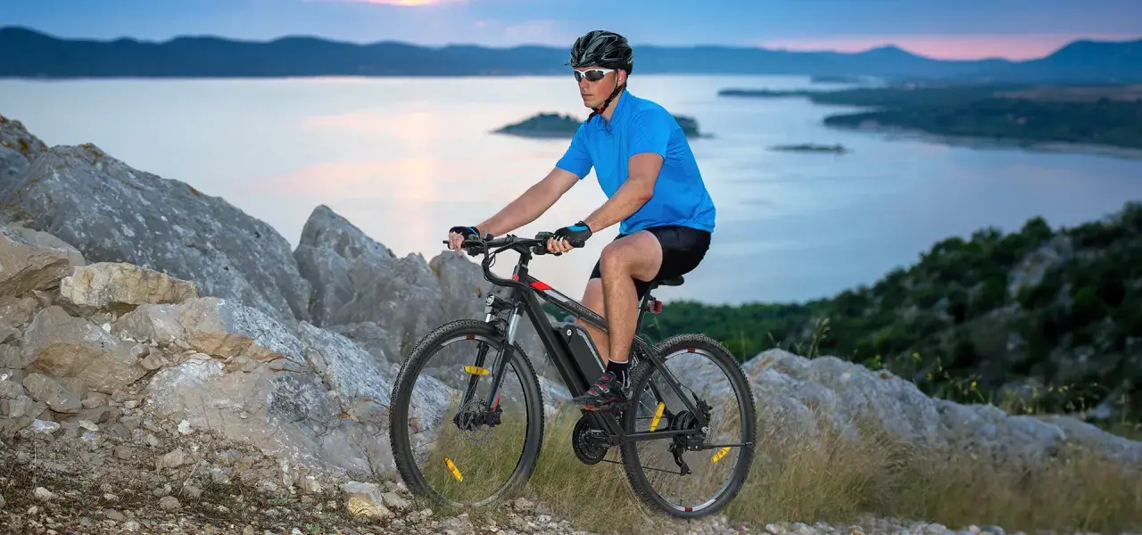 Man riding a mountain bike on a rocky trail overlooking a serene bay at dusk.
