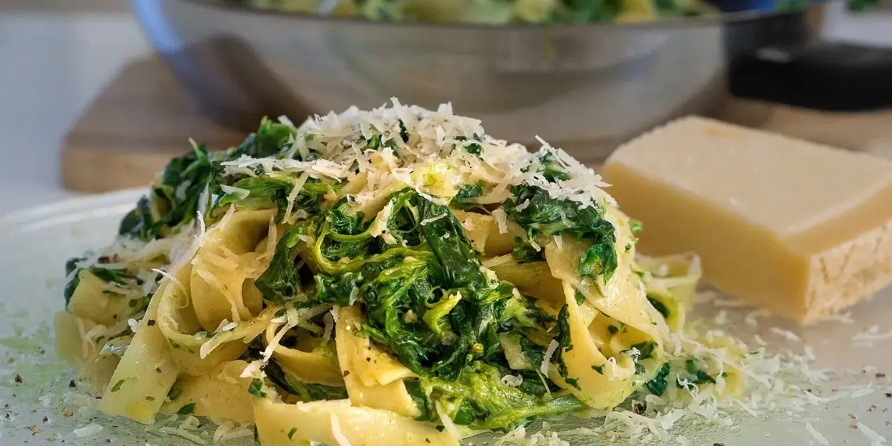 Makaron tagliatelle ze szpinakiem i startym parmezanem, obok kawałek sera.