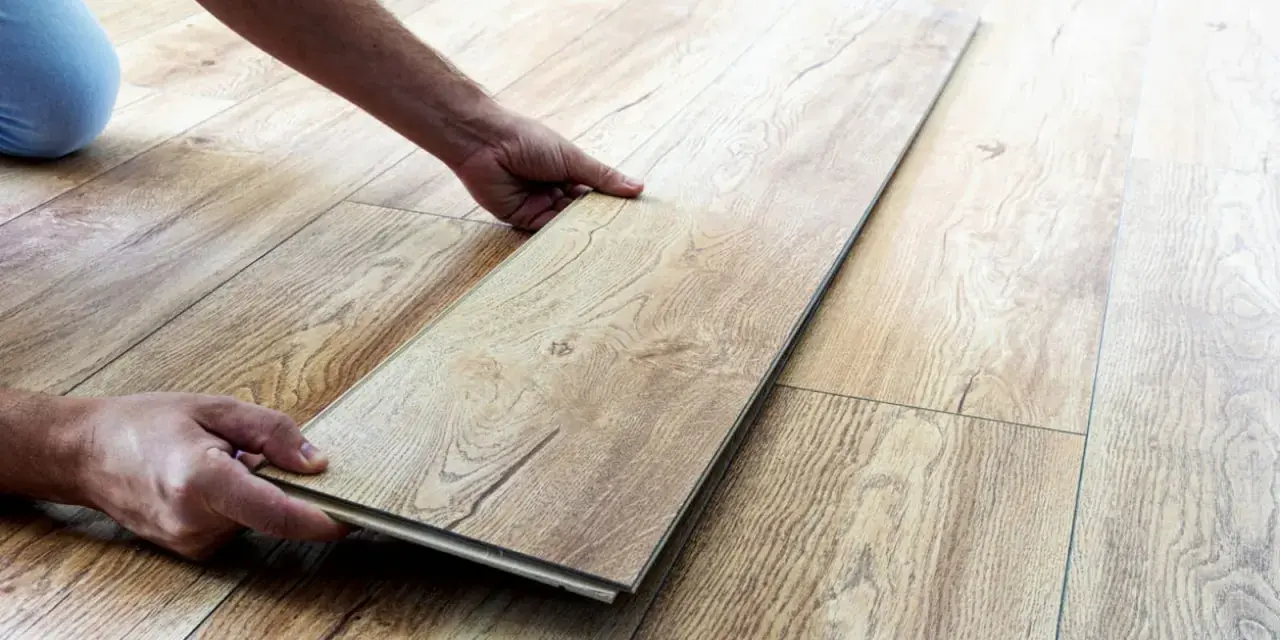 Man's hands placing a laminate plank to repair suelo laminado.