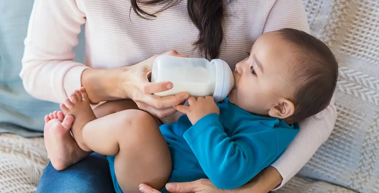 Mama karmi dziecko butelką. To przykład karmienia mieszanego, gdzie dziecko otrzymuje zarówno mleko matki, jak i mleko modyfikowane.