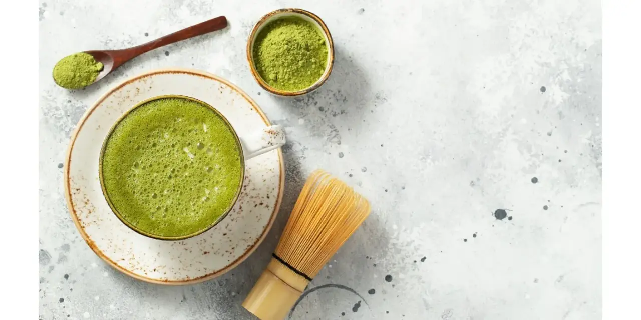 Zielona, spieniona matcha w filiżance, obok bambusowa miotełka i łyżeczka z proszkiem. To właśnie co to matcha – napój pełen energii.