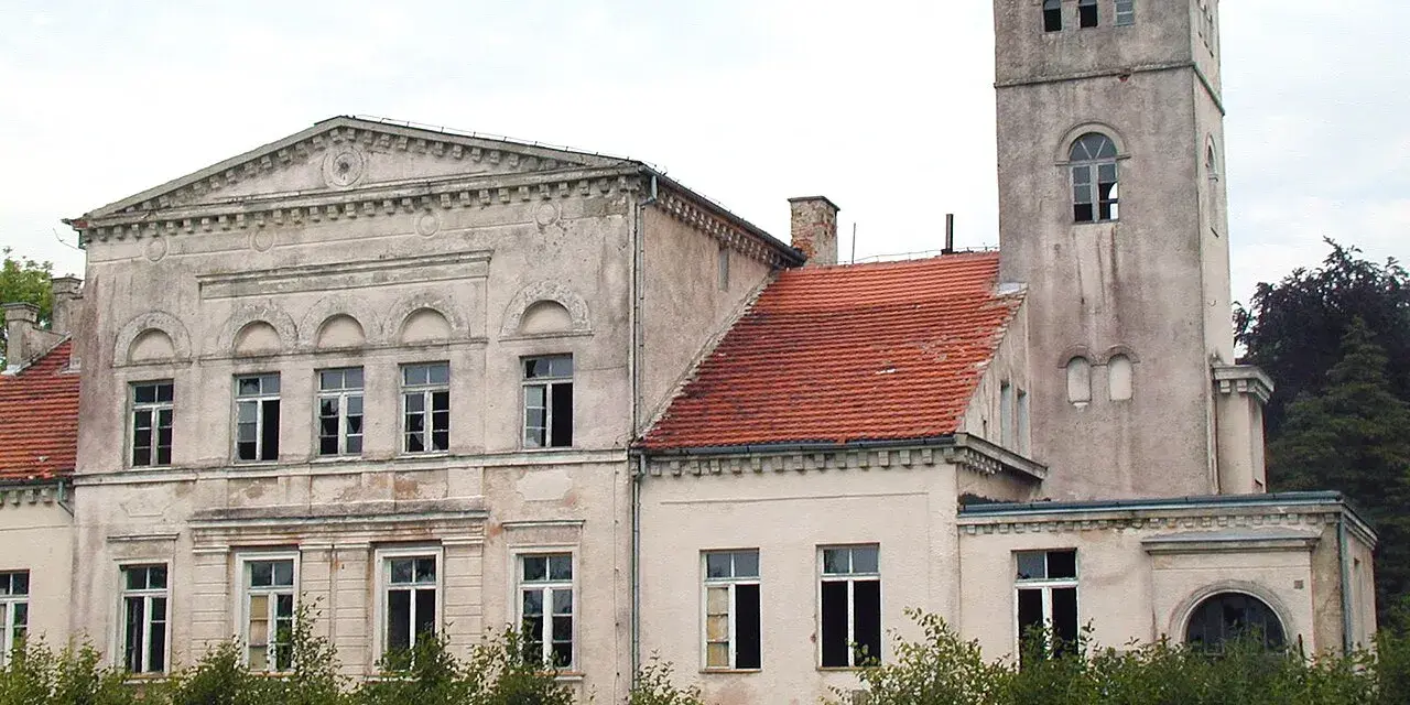 Pałac Rekowo, z wieżą i czerwoną dachówką, otoczony zielenią.