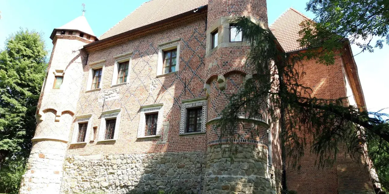 Zamek w Dębnie Polskim, ceglana budowla z kamiennym cokołem, otoczona zielenią.
