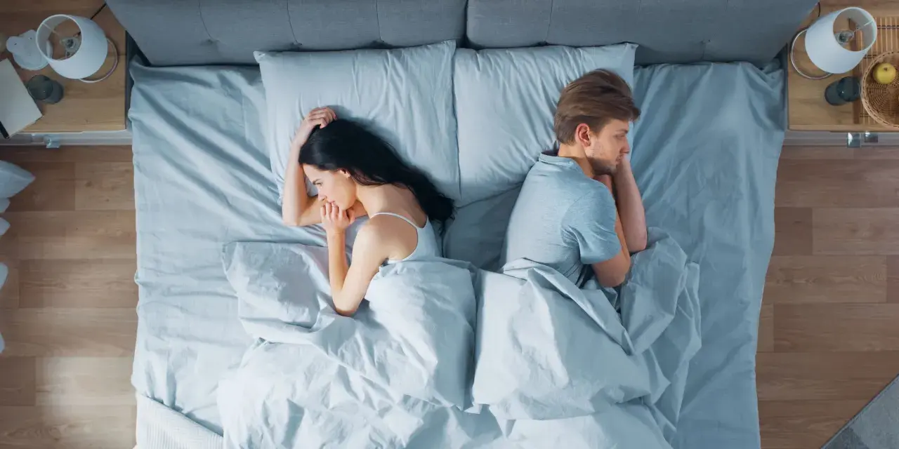 Ein Paar liegt im Bett, jeder auf seiner Seite, die Rücken einander zugewandt. Getrennte Schlafzimmer – der Anfang vom Ende?