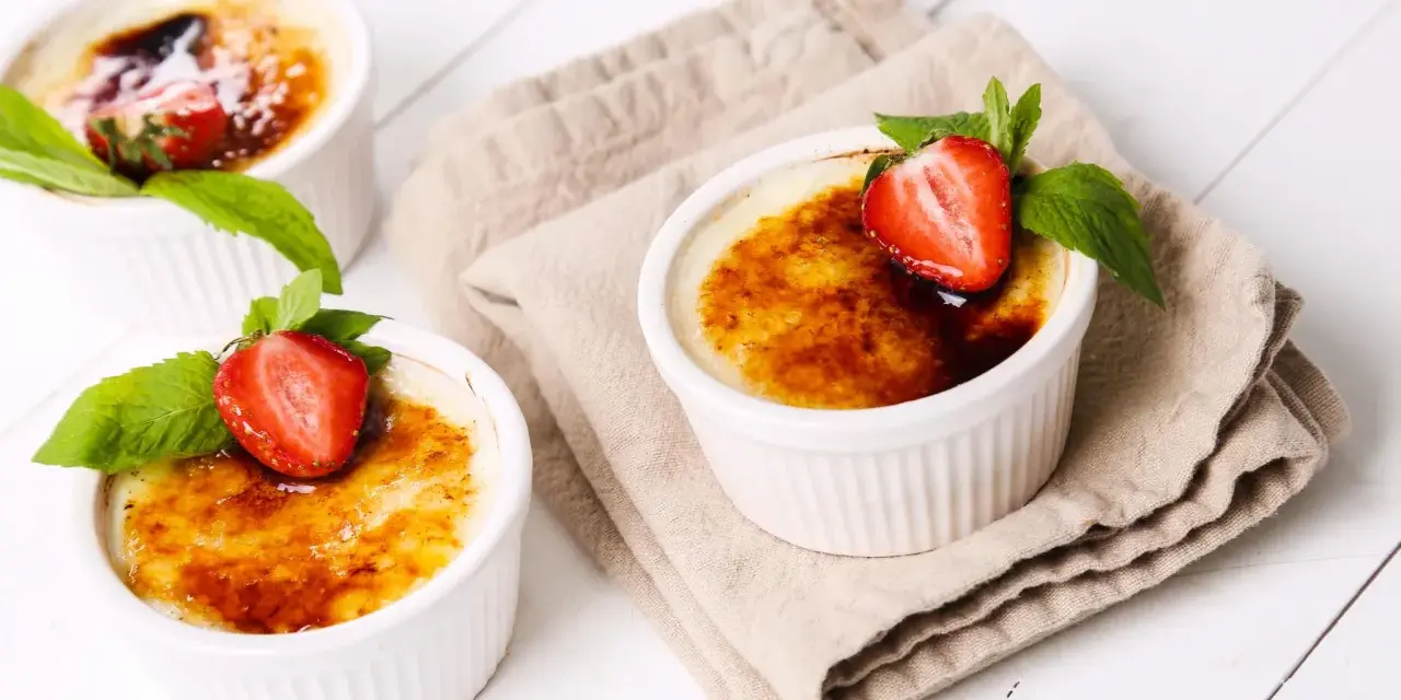 Trzy kremowe desery, Crème brûlée czy crema catalana, ozdobione truskawkami i miętą, kuszą skarmelizowanym cukrem.