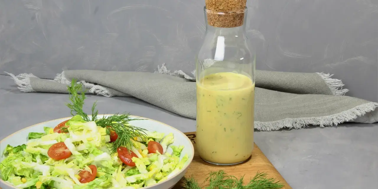 Frischer Salat mit Tomaten und Mais, daneben eine Flasche mit cremigem Jogurt Dressing und Dill.