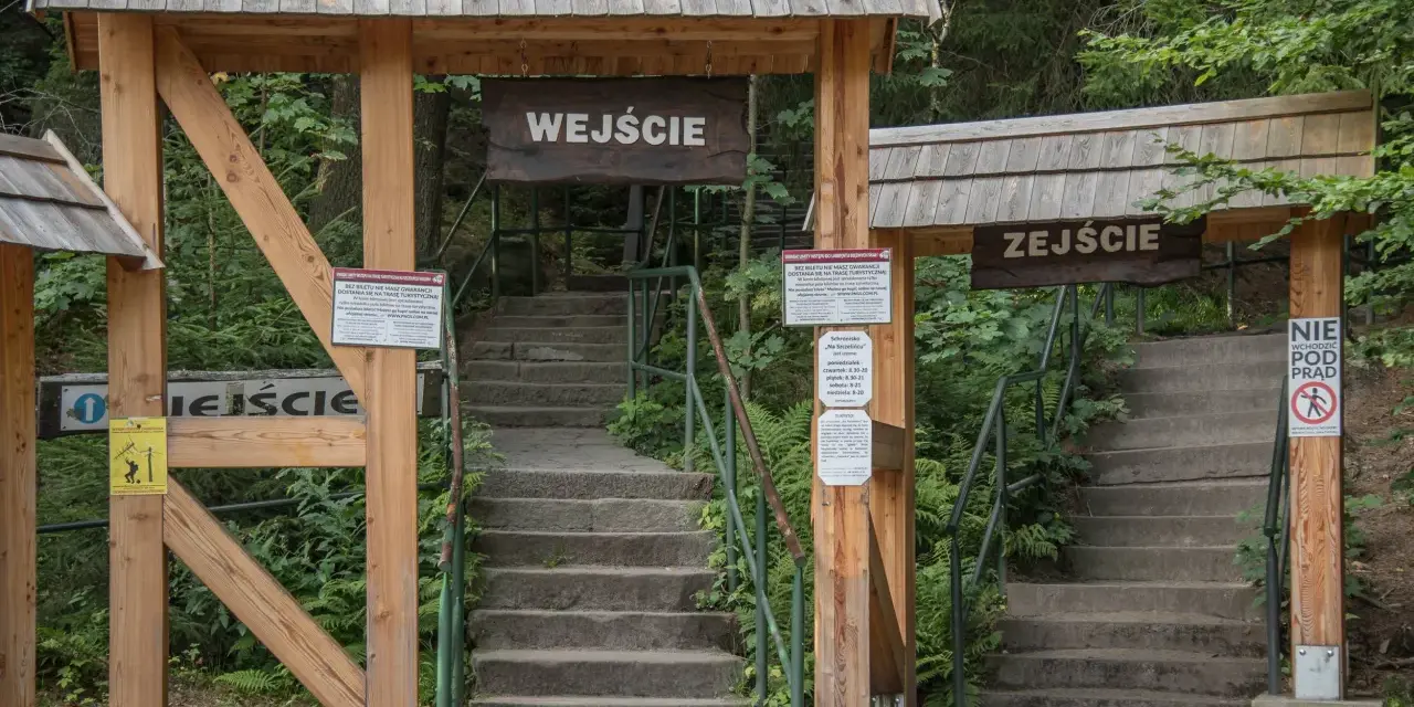 Kamienne schody prowadzą do wejścia na trasę turystyczną w Szczelińcu Wielkim. Po prawej stronie znajduje się znak "Zejście" i zakaz wchodzenia pod prąd.